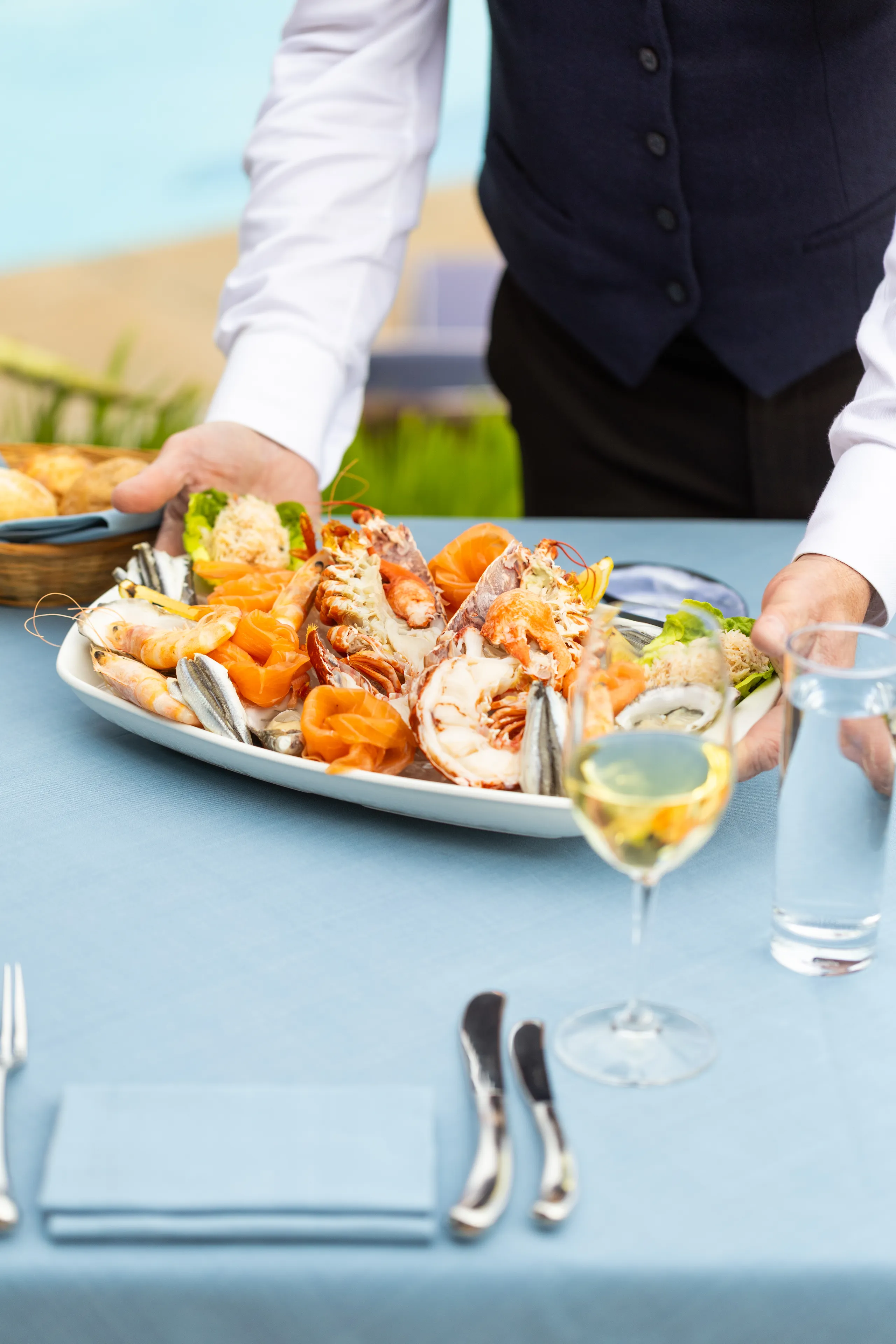 Server placing a seafood platter with lobster, prawns and salmon on a restaurant table