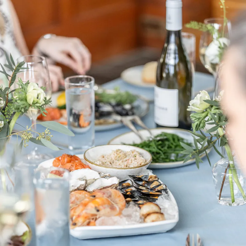 Elegant seafood spread on a softly styled dining table with white wine, oysters, prawns and mussels on ice