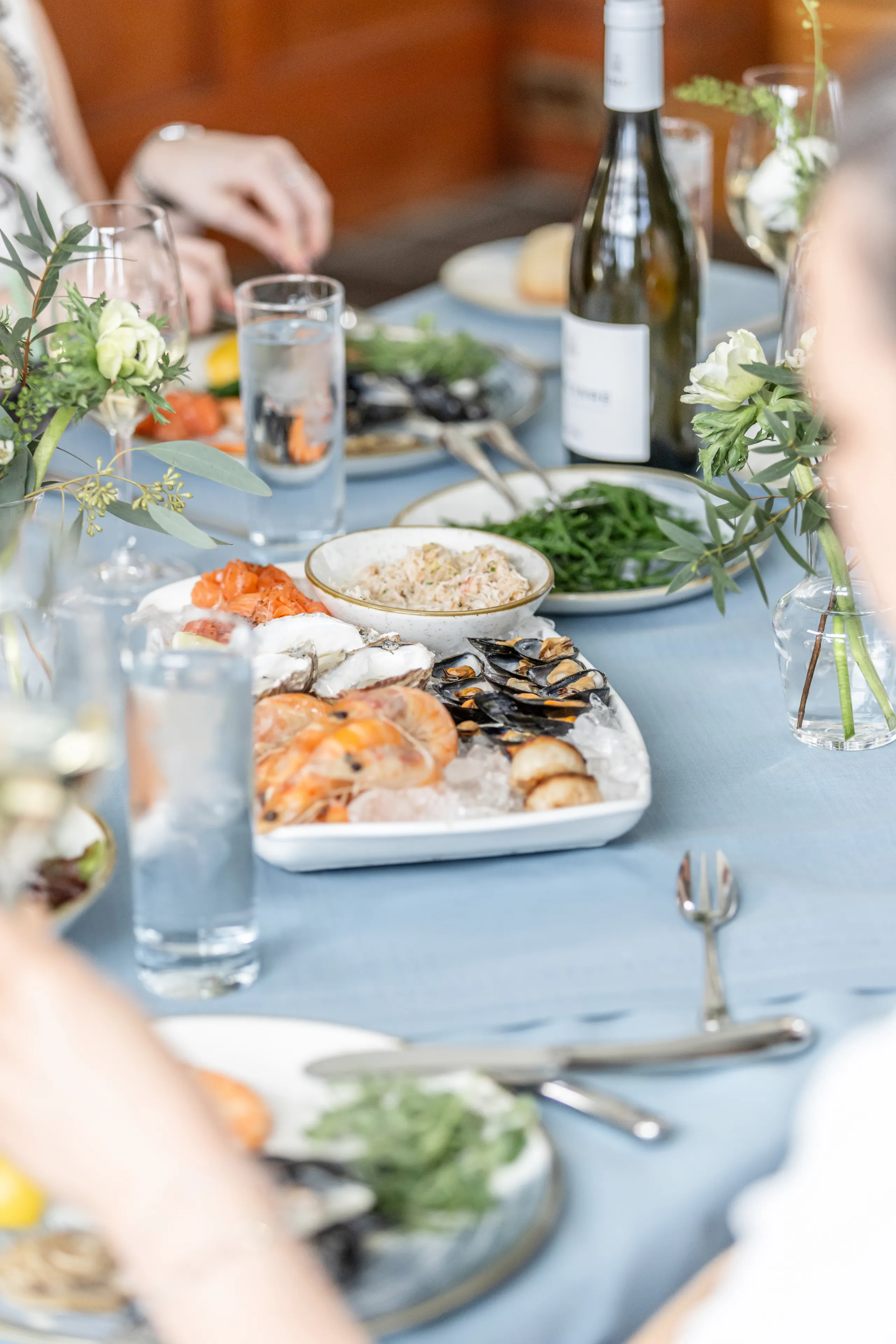 Elegant seafood spread on a softly styled dining table with white wine, oysters, prawns and mussels on ice