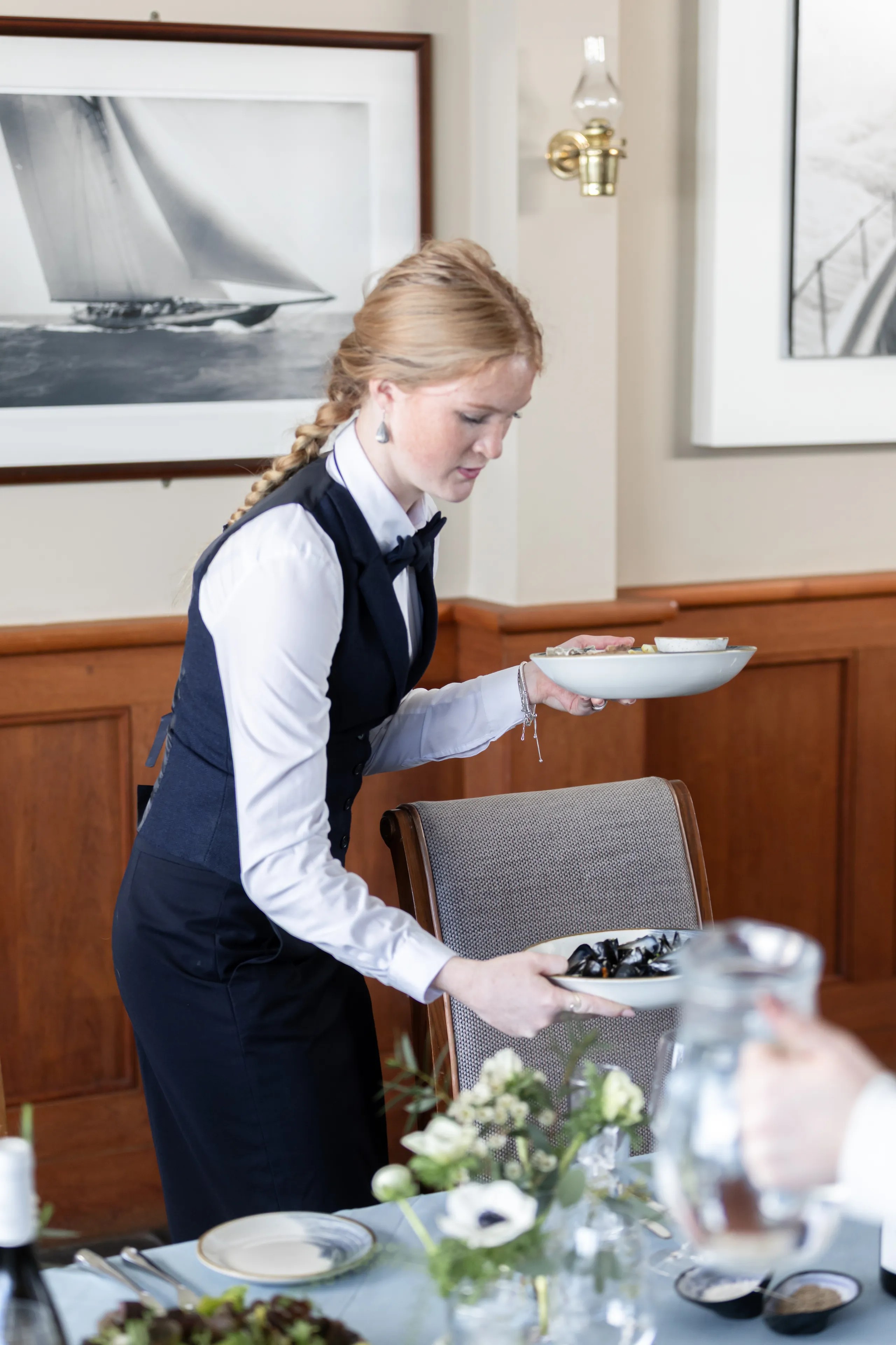 Waitress serving dishes at a restaurant table in a refined dining room