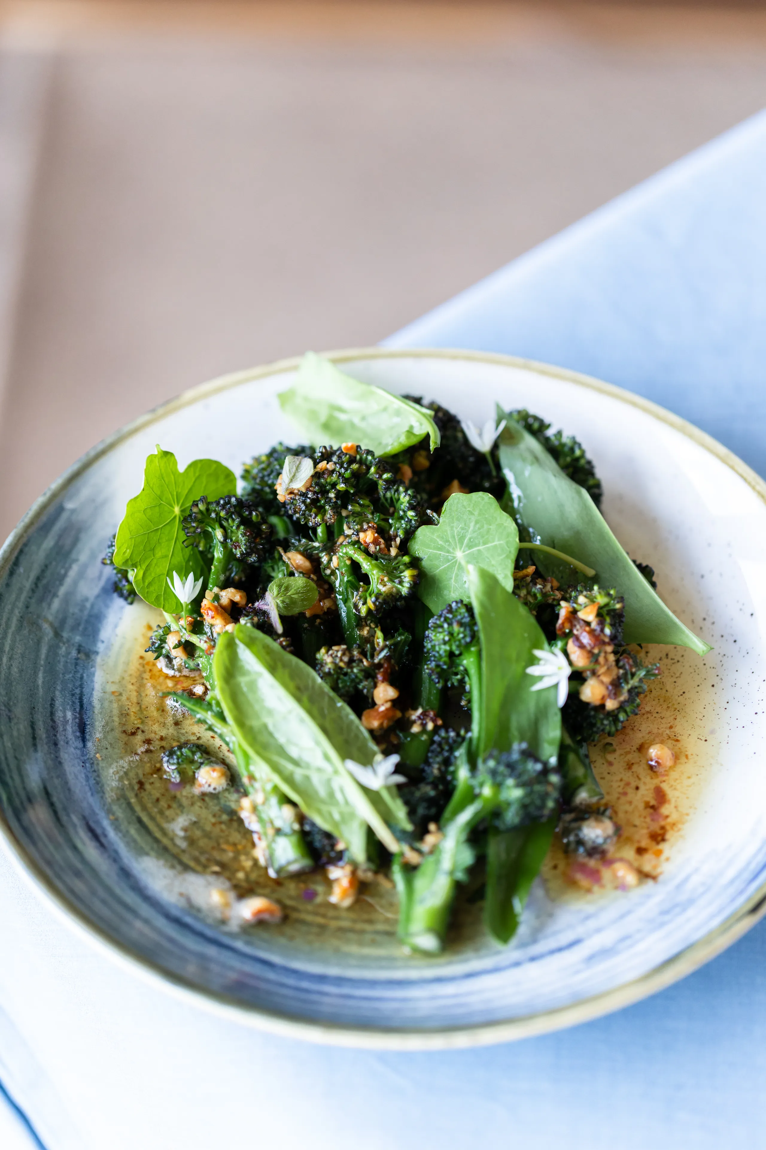 Bowl of charred tenderstem broccoli with leafy greens, edible flowers and a nutty dressing