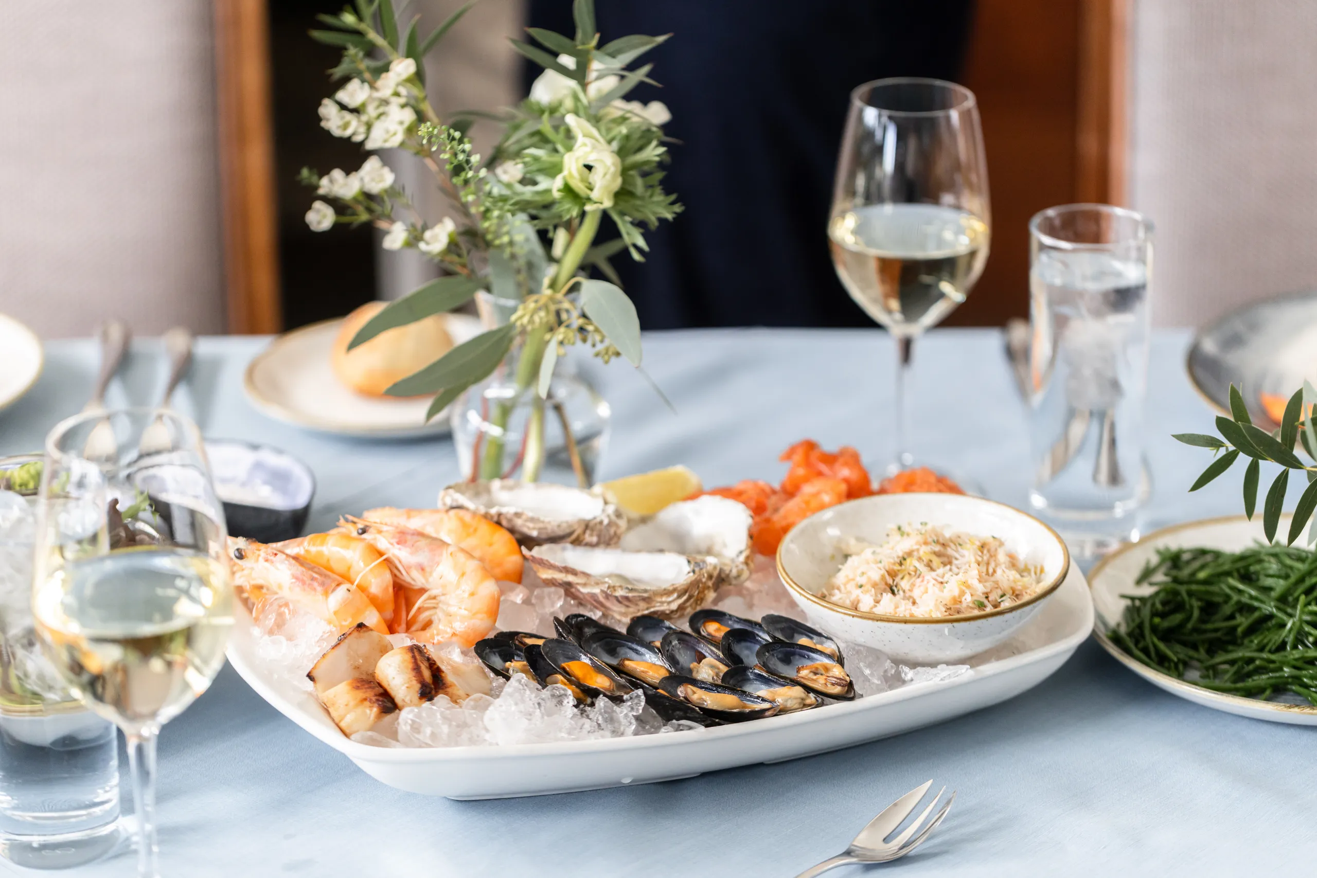 Seafood platter on ice with prawns, mussels and oysters, served with white wine on a neatly dressed dining table