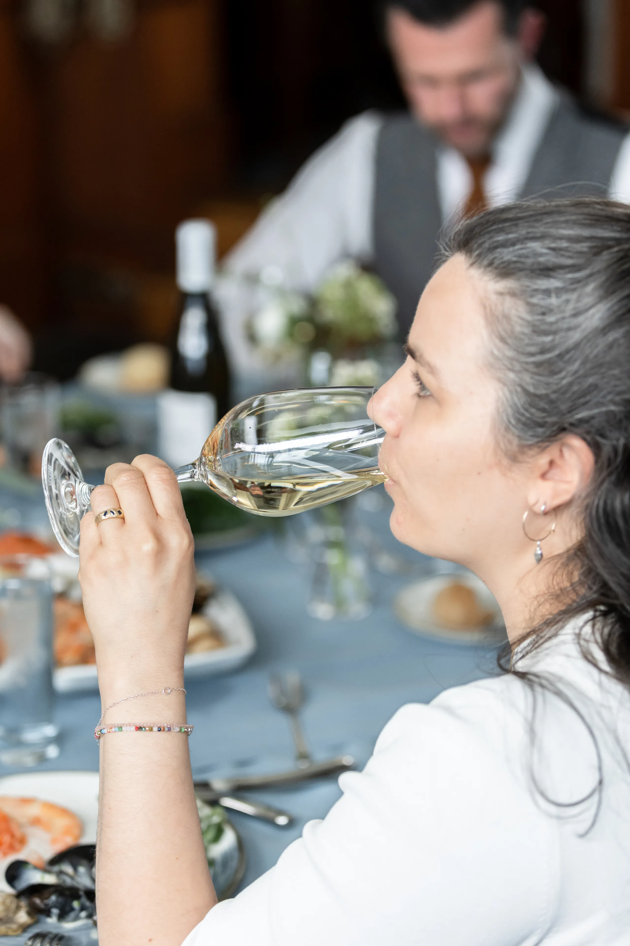 Woman sipping white wine at a restaurant table during a meal