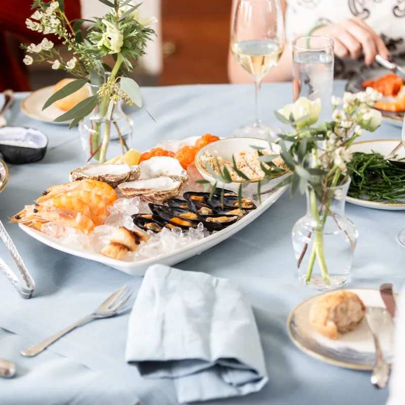 Elegant seafood dining table with prawns, oysters and mussels served on ice, surrounded by salads, wine glasses and small floral arrangements
