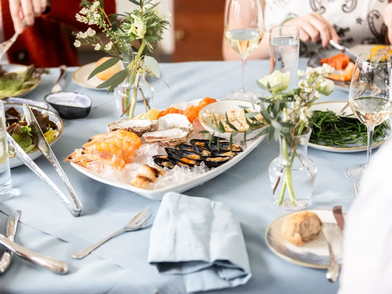 Elegant seafood dining table with prawns, oysters and mussels served on ice, surrounded by salads, wine glasses and small floral arrangements