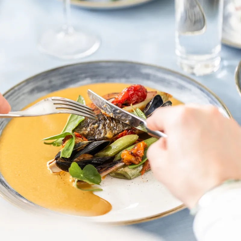 Fine dining plate with seafood and vegetables being cut with knife and fork at an elegant table setting