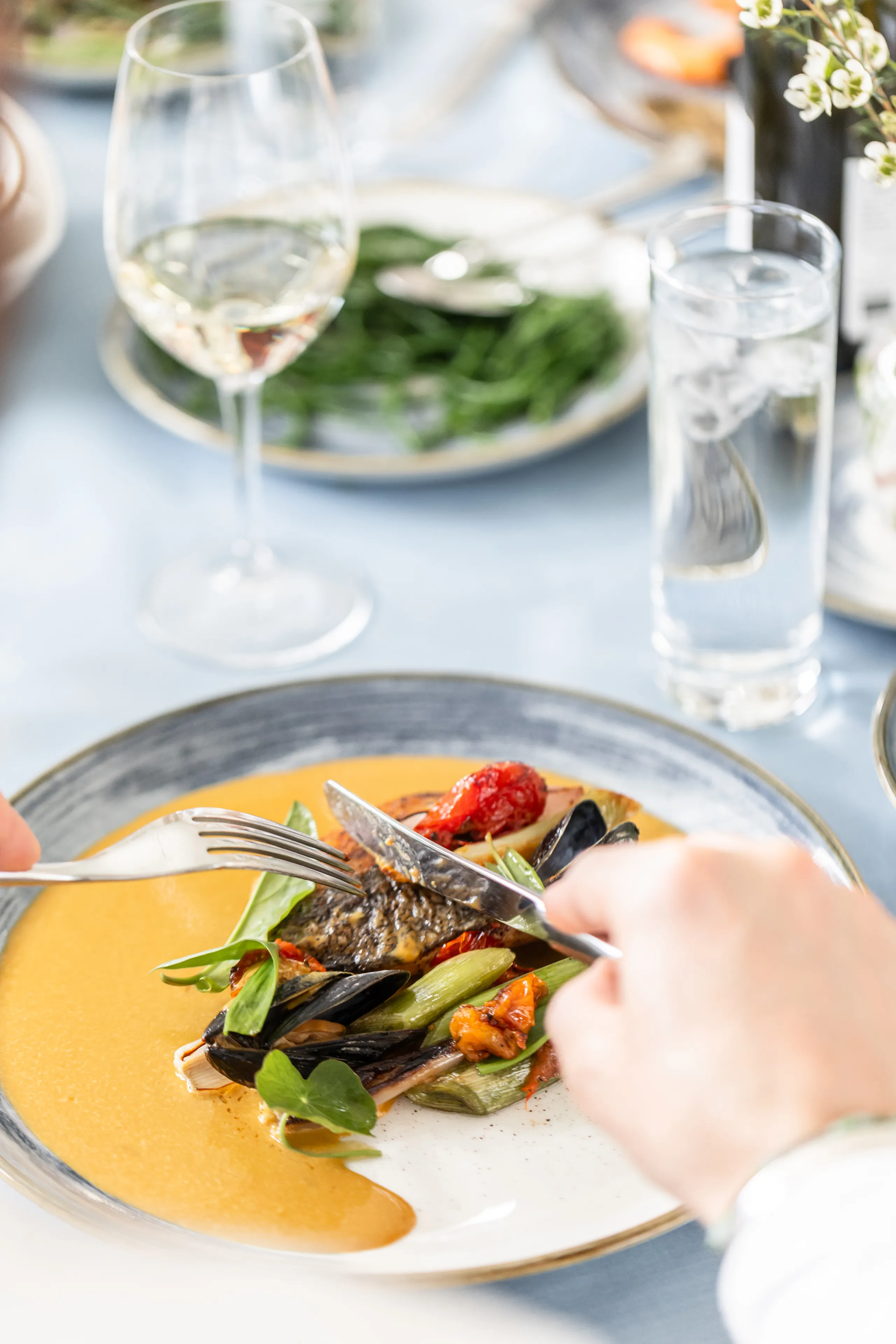 Fine dining plate with seafood and vegetables being cut with knife and fork at an elegant table setting