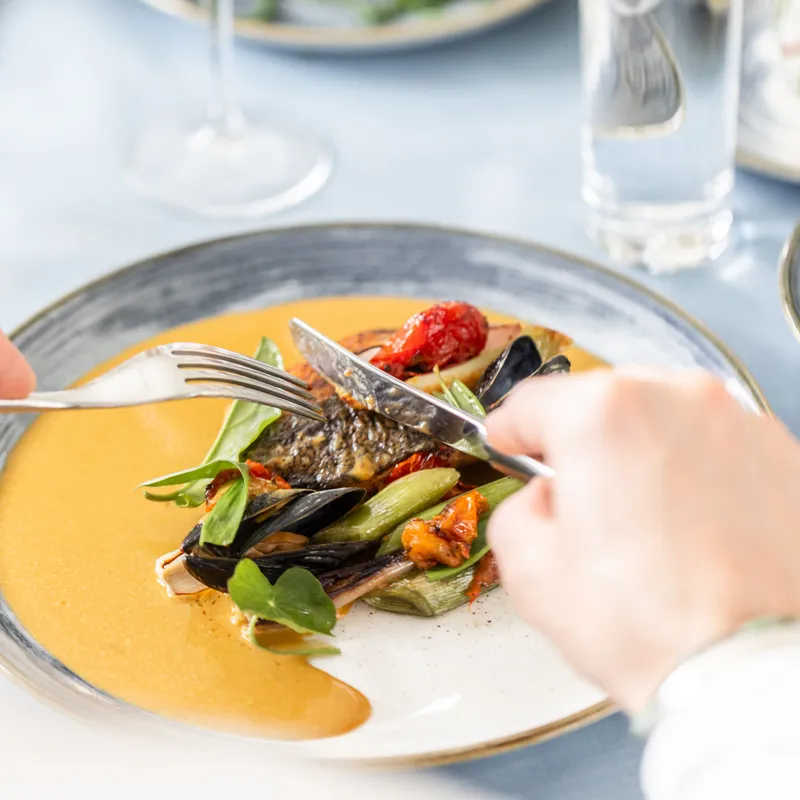 Fine dining plate with seafood and vegetables being cut with knife and fork at an elegant table setting