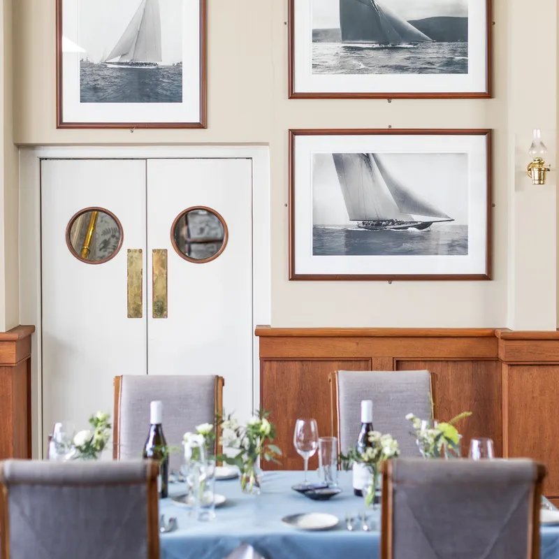 Elegant dining room with a laid table, framed sailing photographs and white double doors with round porthole windows.