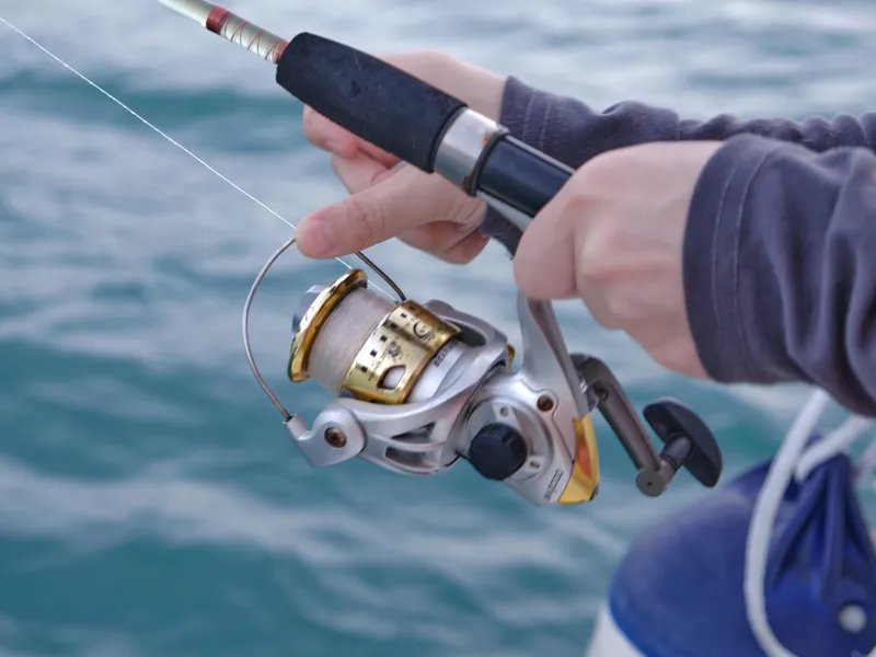 Close-up of a person holding a fishing rod and reel over the sea