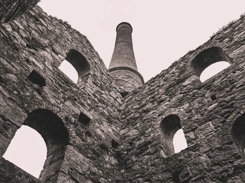 Low-angle view of weathered stone ruins with arched windows and a tall chimney rising into the sky