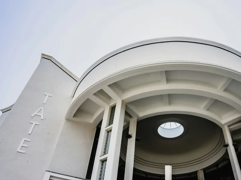 Tate St Ives Low-angle view of a white Art Deco style building entrance with curved columns and the word 'TATE' on the wall.