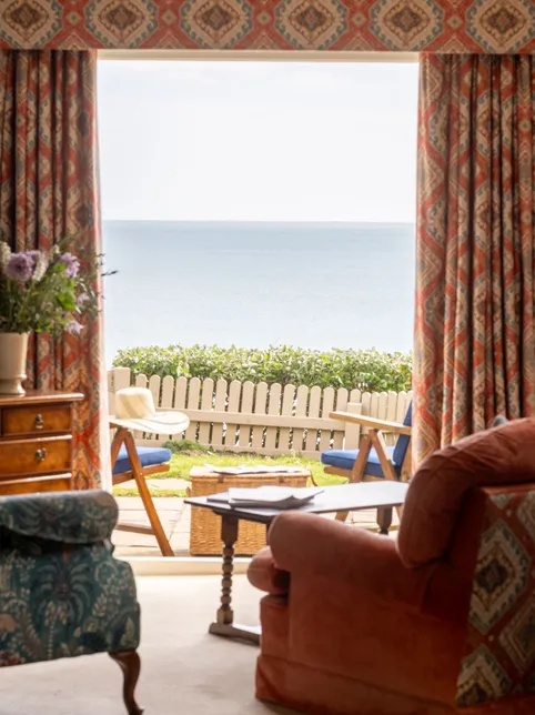 Cosy living room with patterned curtains opening onto a seaside patio and calm sea view
