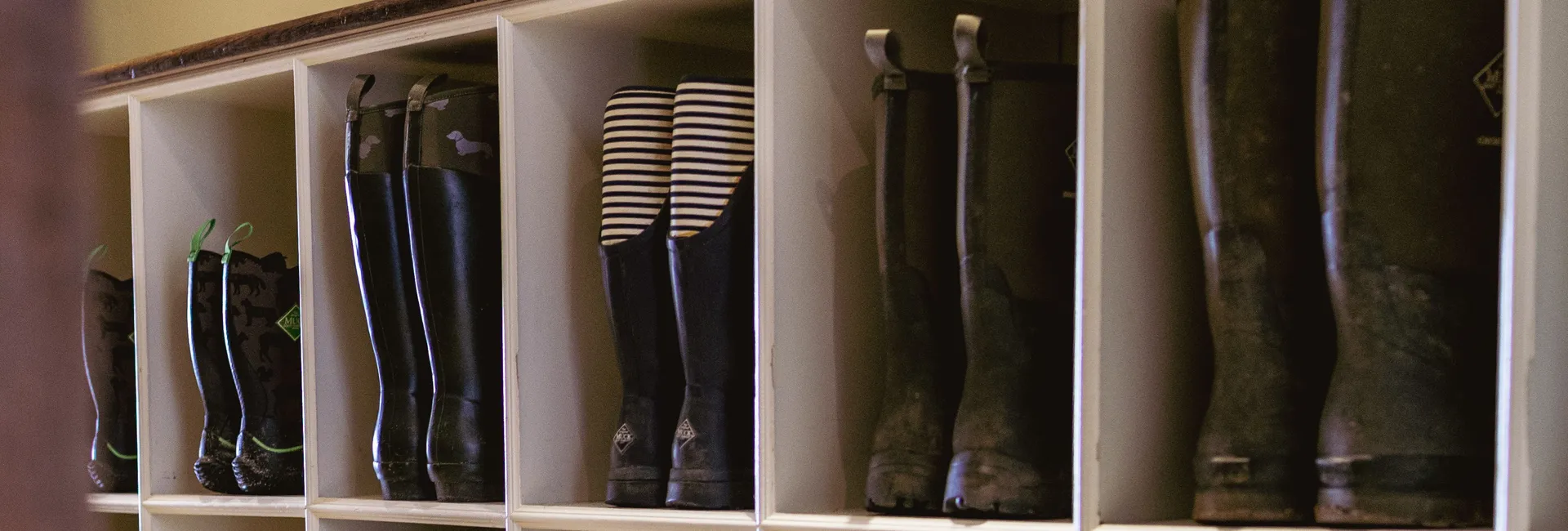 White cubby storage filled with Wellington boots beneath a Muck Boot Company sign in a hallway.