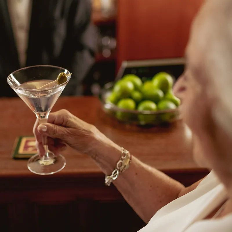 Older woman holding a martini with an olive at a bar counter
