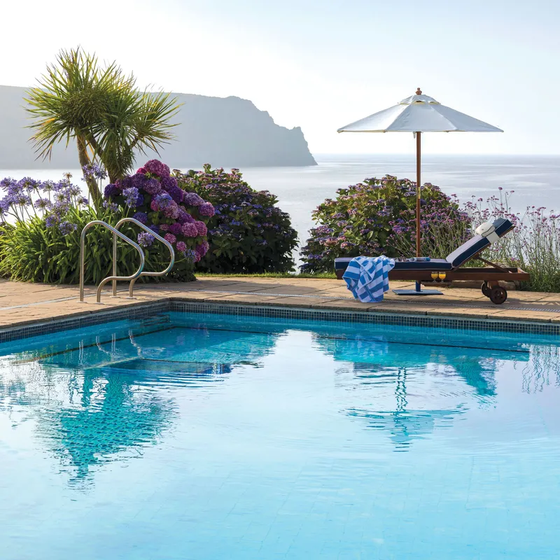 Outdoor swimming pool with a sun lounger and parasol overlooking the sea and coastal cliffs