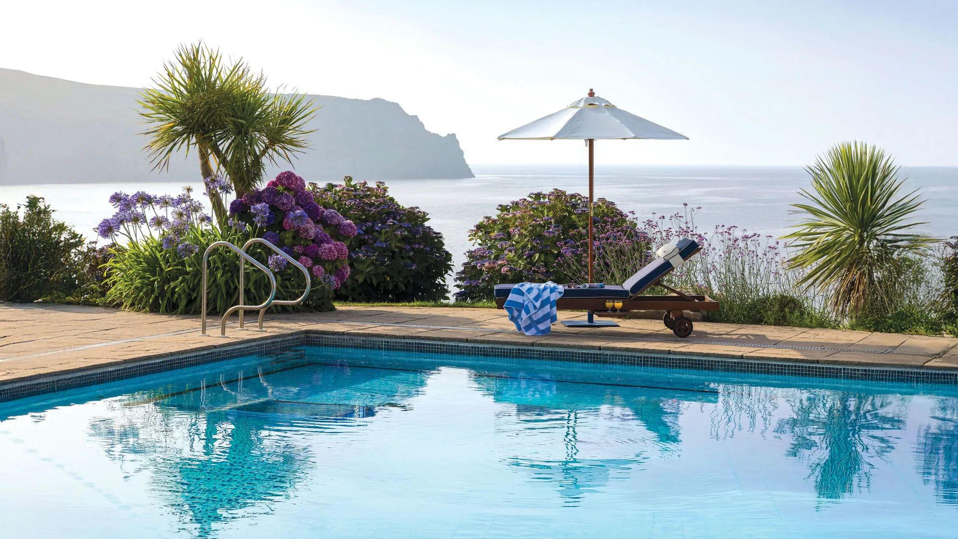 Outdoor swimming pool with a sun lounger and parasol overlooking the sea and coastal cliffs