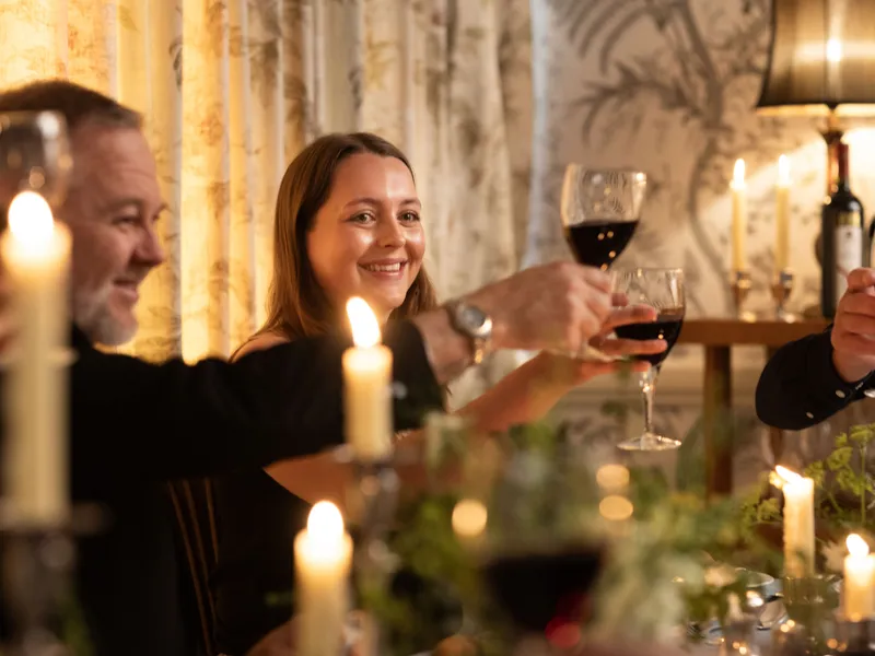 Friends toasting with glasses of red wine at a candlelit dinner table