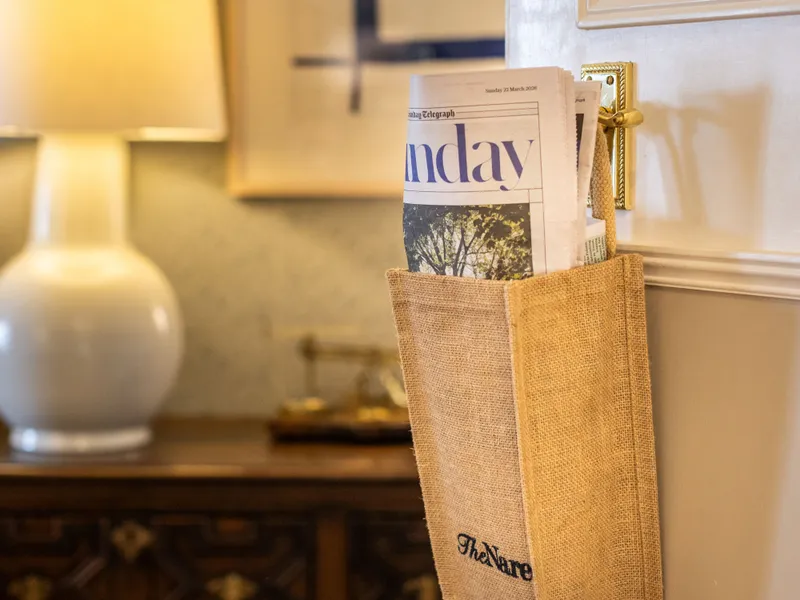 Newspaper holder hanging from a brass door handle in a warmly lit hotel room