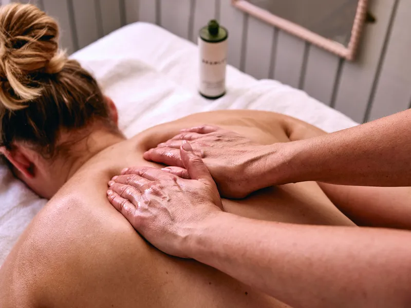 Close-up of a therapist giving an oil massage to a client’s upper back in a treatment room.