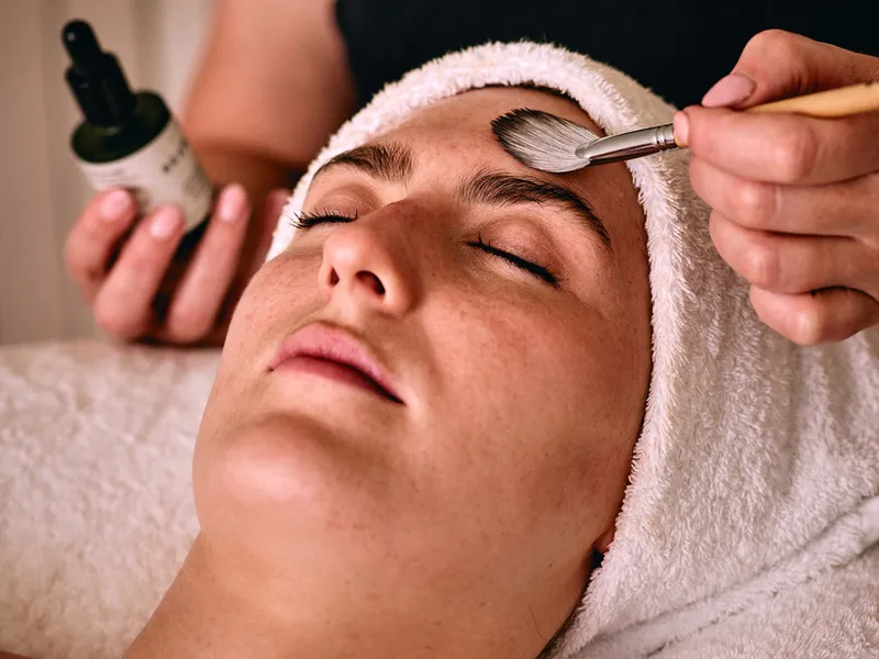 Spa therapist applying a facial treatment with a brush to a reclining client