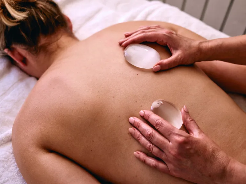 Therapist giving a warm stone massage to a client's back in a treatment room