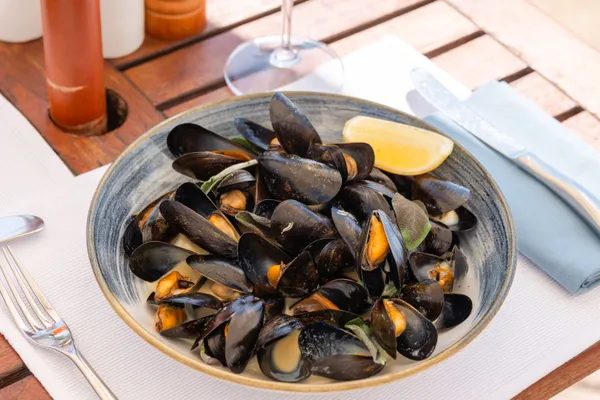 Bowl of steamed mussels with lemon beside a mint cocktail on an outdoor table