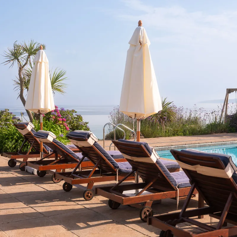 Sun loungers and closed parasols beside an outdoor pool overlooking the sea