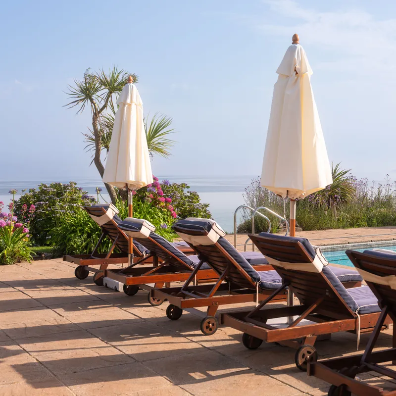 Sun loungers and closed parasols beside an outdoor pool overlooking the sea