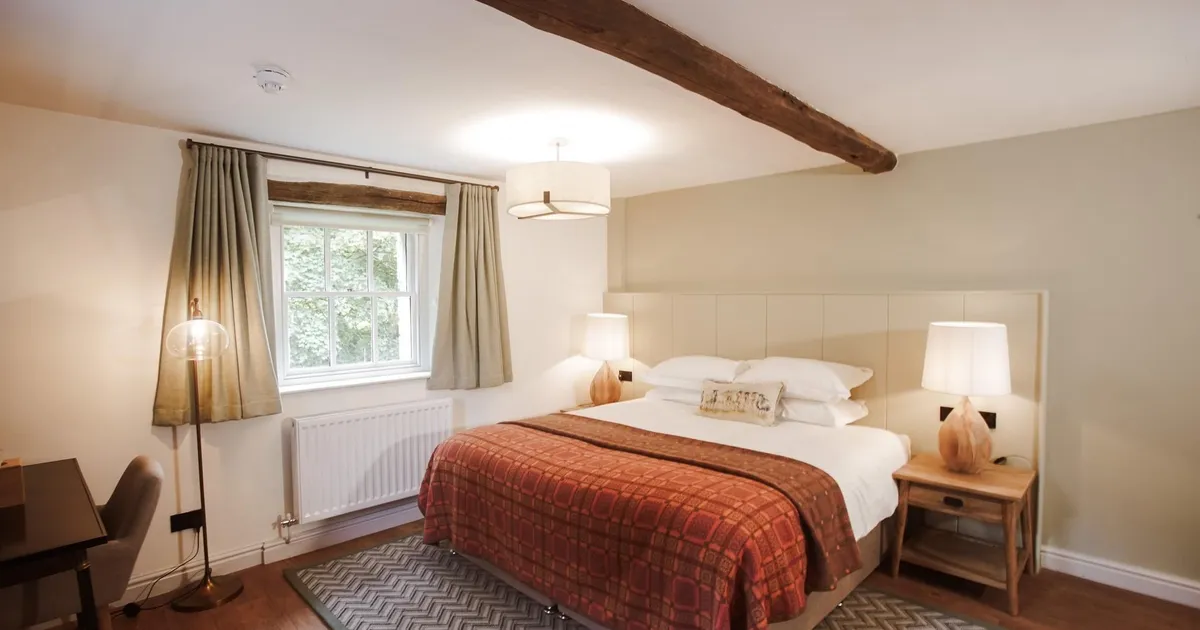 Cosy bedroom with a double bed, red patterned throw, wooden beams and bedside lamps.