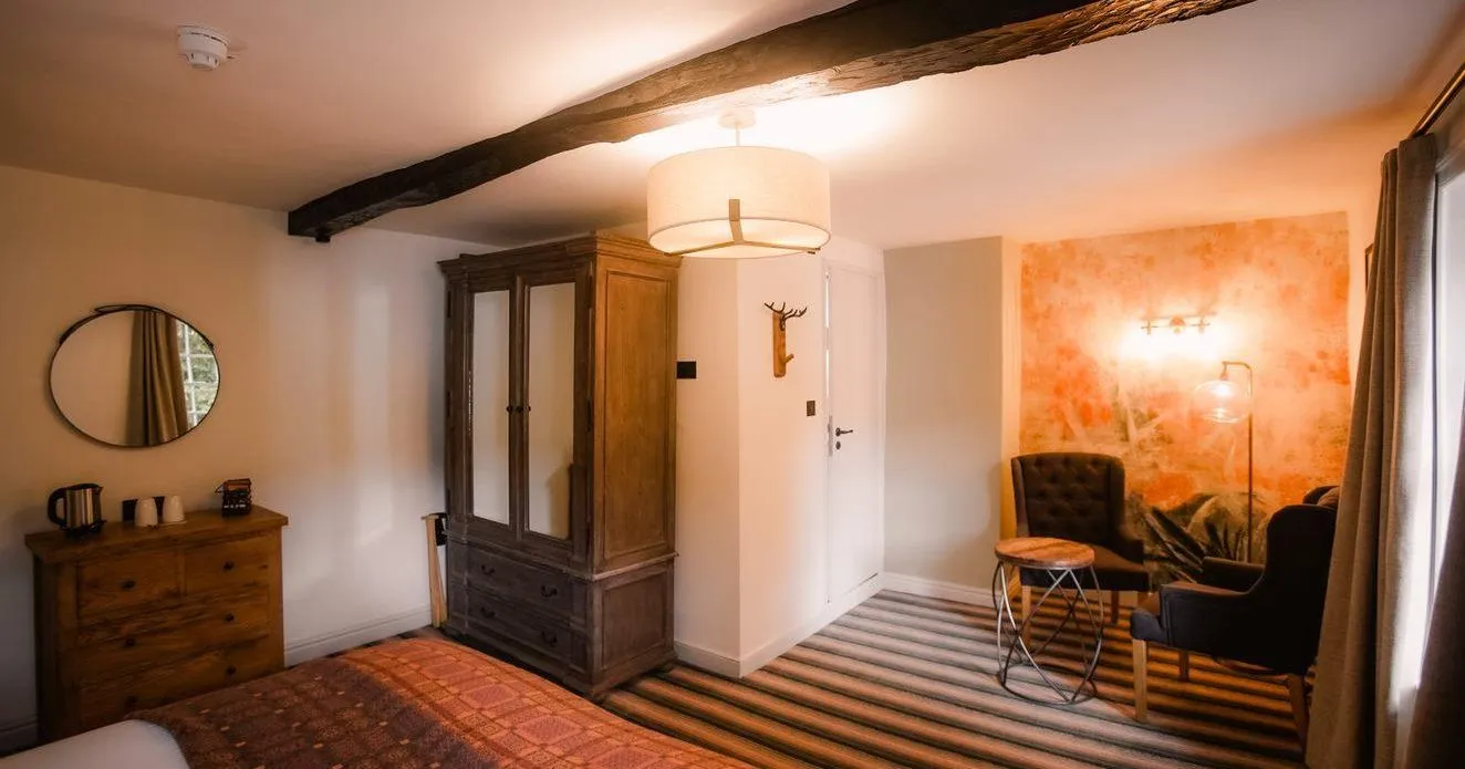 Cosy rustic bedroom with exposed wooden beams, antique wardrobe and armchairs