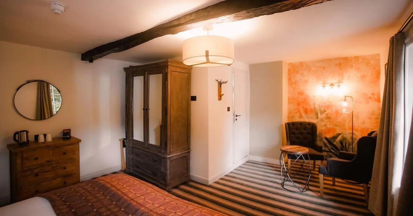 Cosy rustic bedroom with exposed wooden beams, antique wardrobe and armchairs