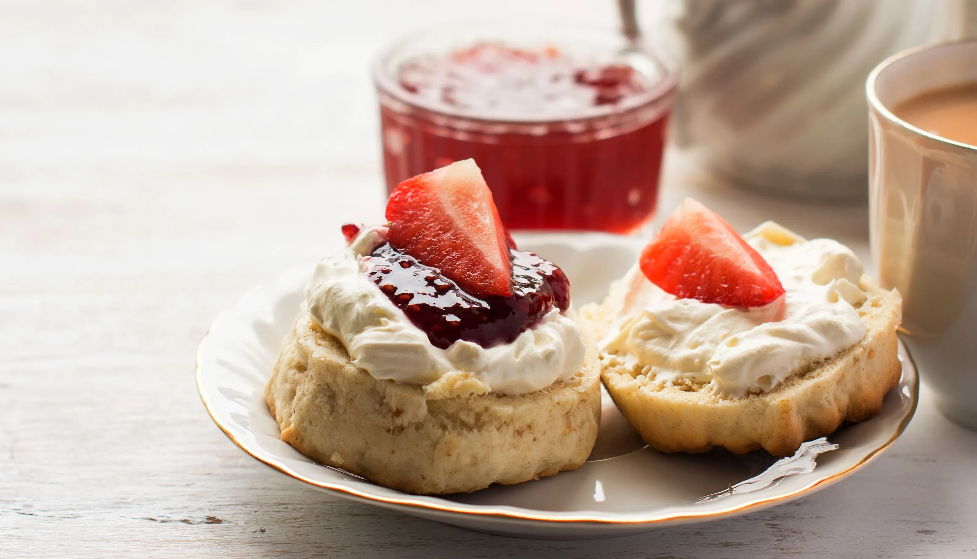 Cream tea with scones topped with clotted cream, strawberry jam and fresh strawberries beside a teapot and cup
