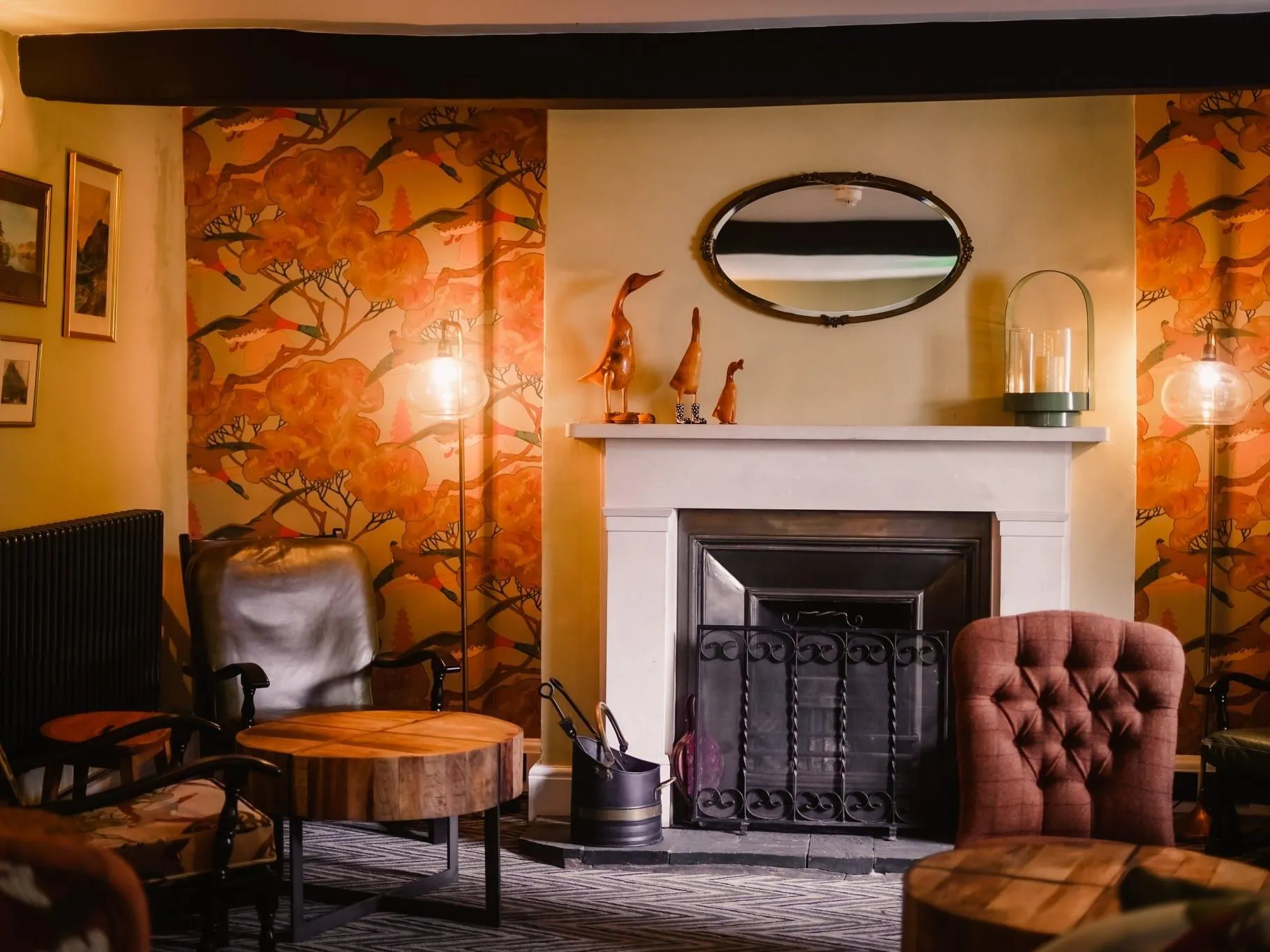 Cosy lounge with a fireplace, patterned orange wallpaper, leather chairs and warm lamps