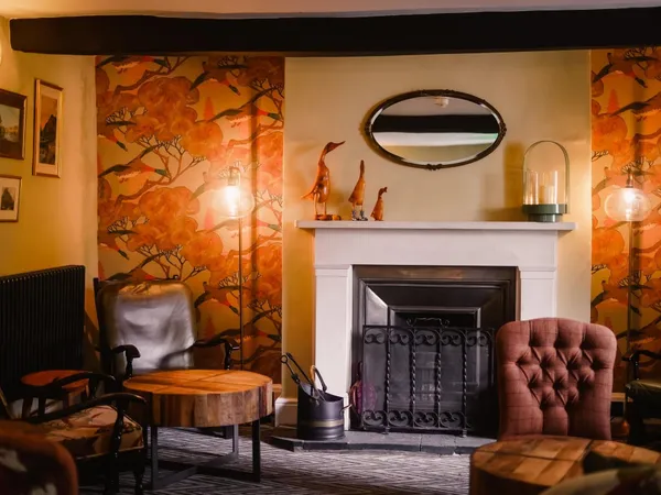 Cosy lounge with a fireplace, patterned orange wallpaper, leather chairs and warm lamps