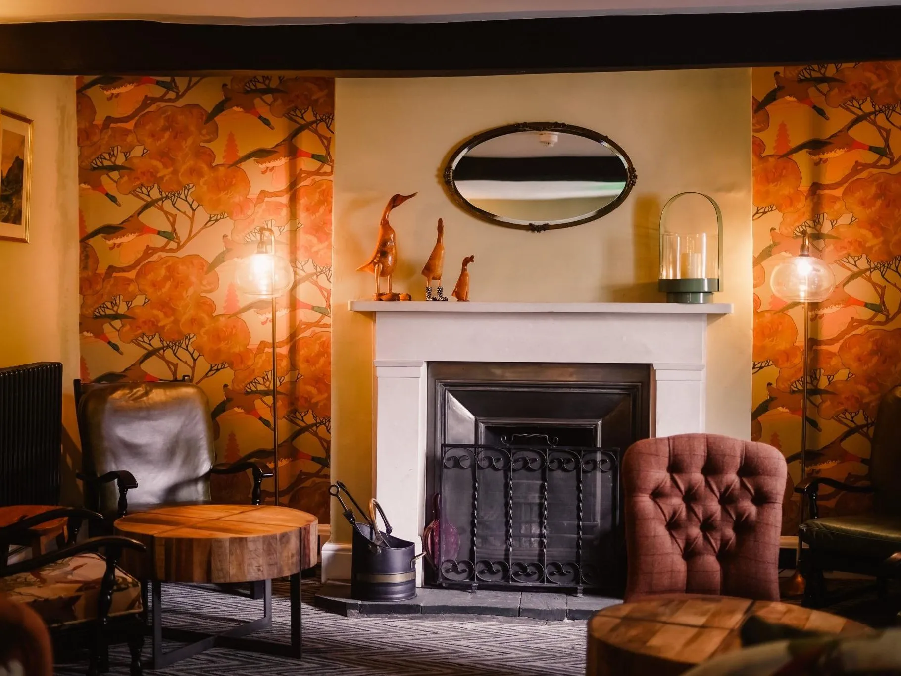 Cosy lounge with a fireplace, patterned orange wallpaper, leather chairs and warm lamps