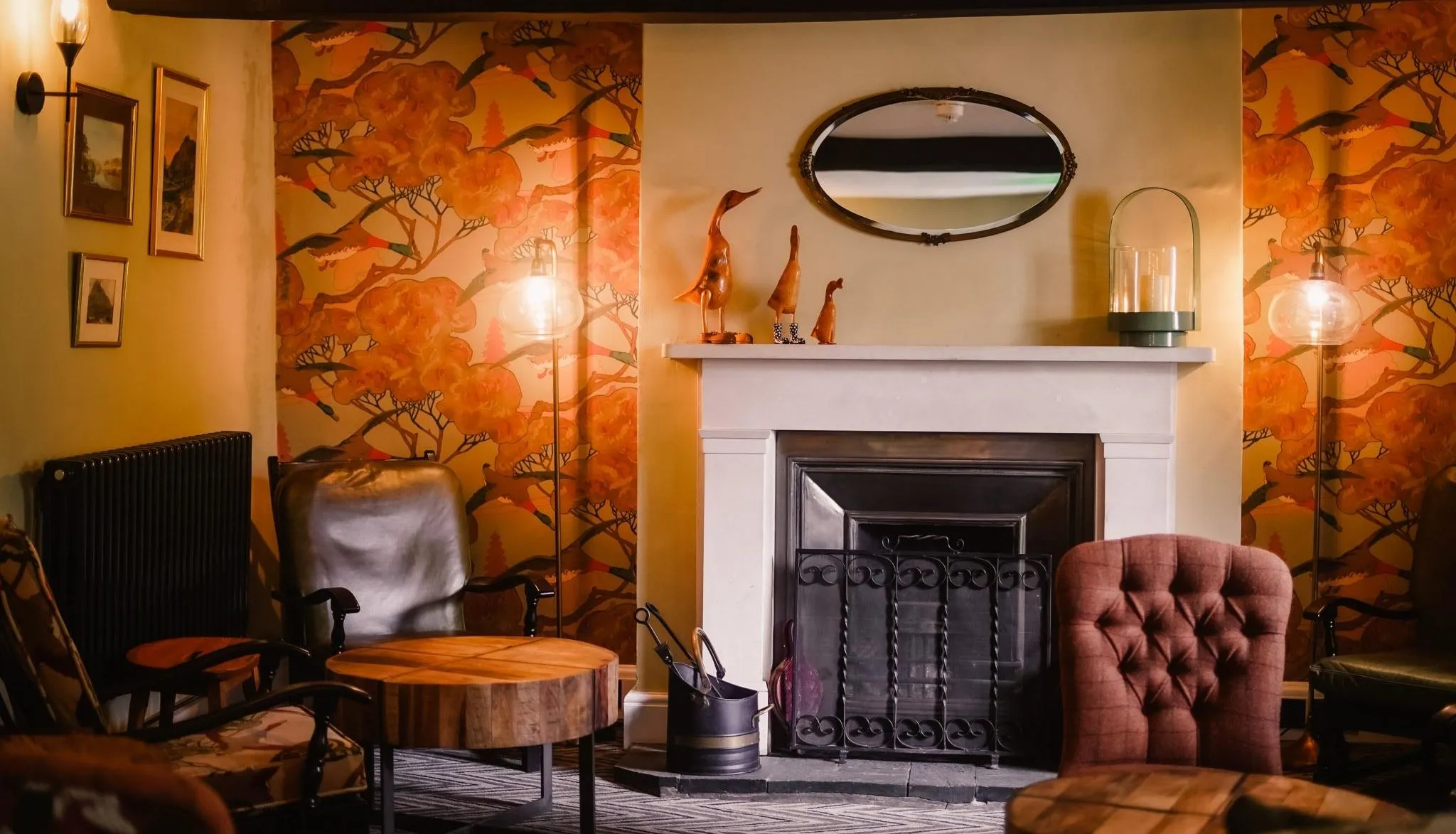 Cosy lounge with a fireplace, patterned orange wallpaper, leather chairs and warm lamps