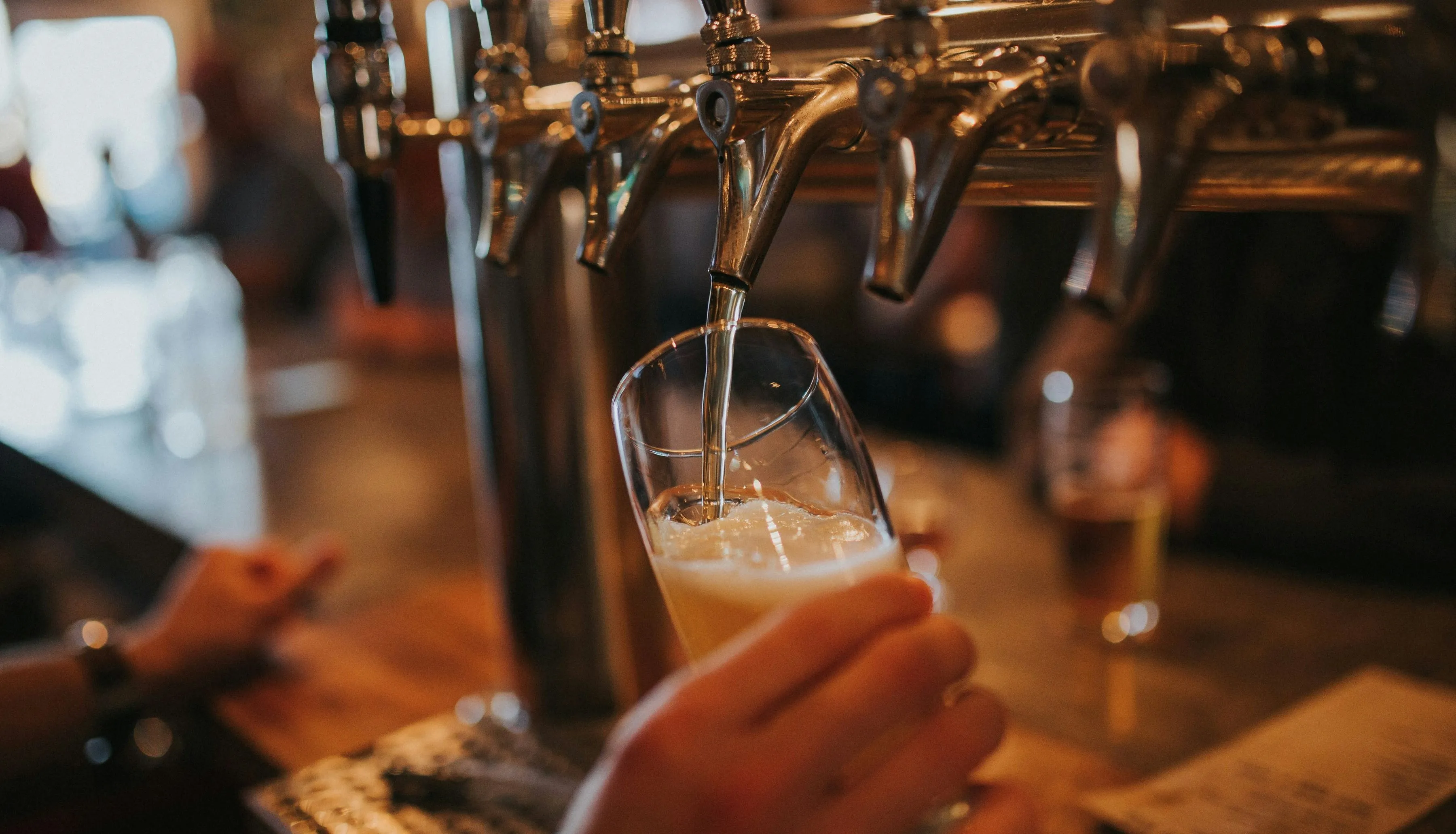 A bartender pours pale beer from a polished brass tap into a tilted pint glass.