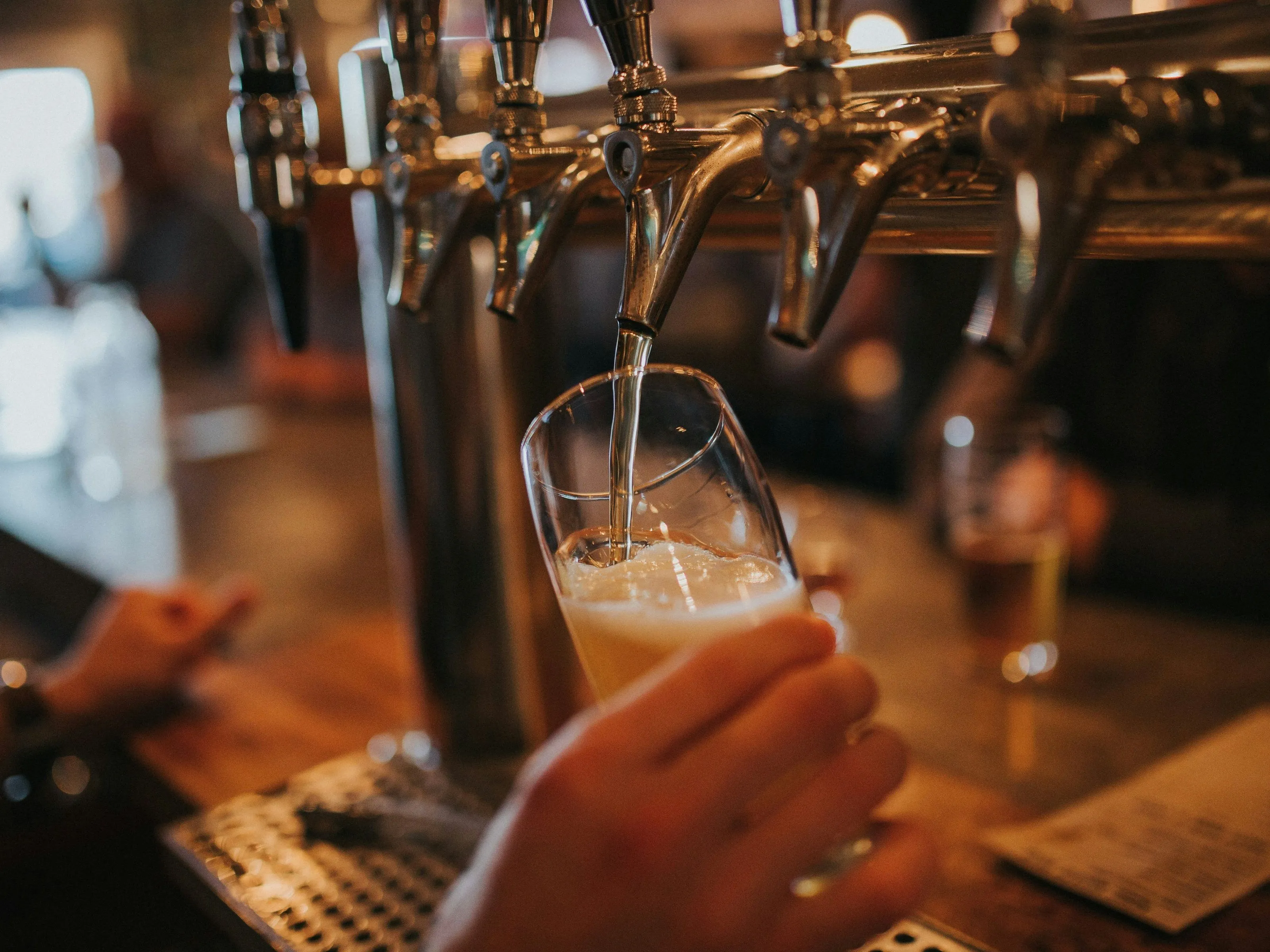 A bartender pours pale beer from a polished brass tap into a tilted pint glass.