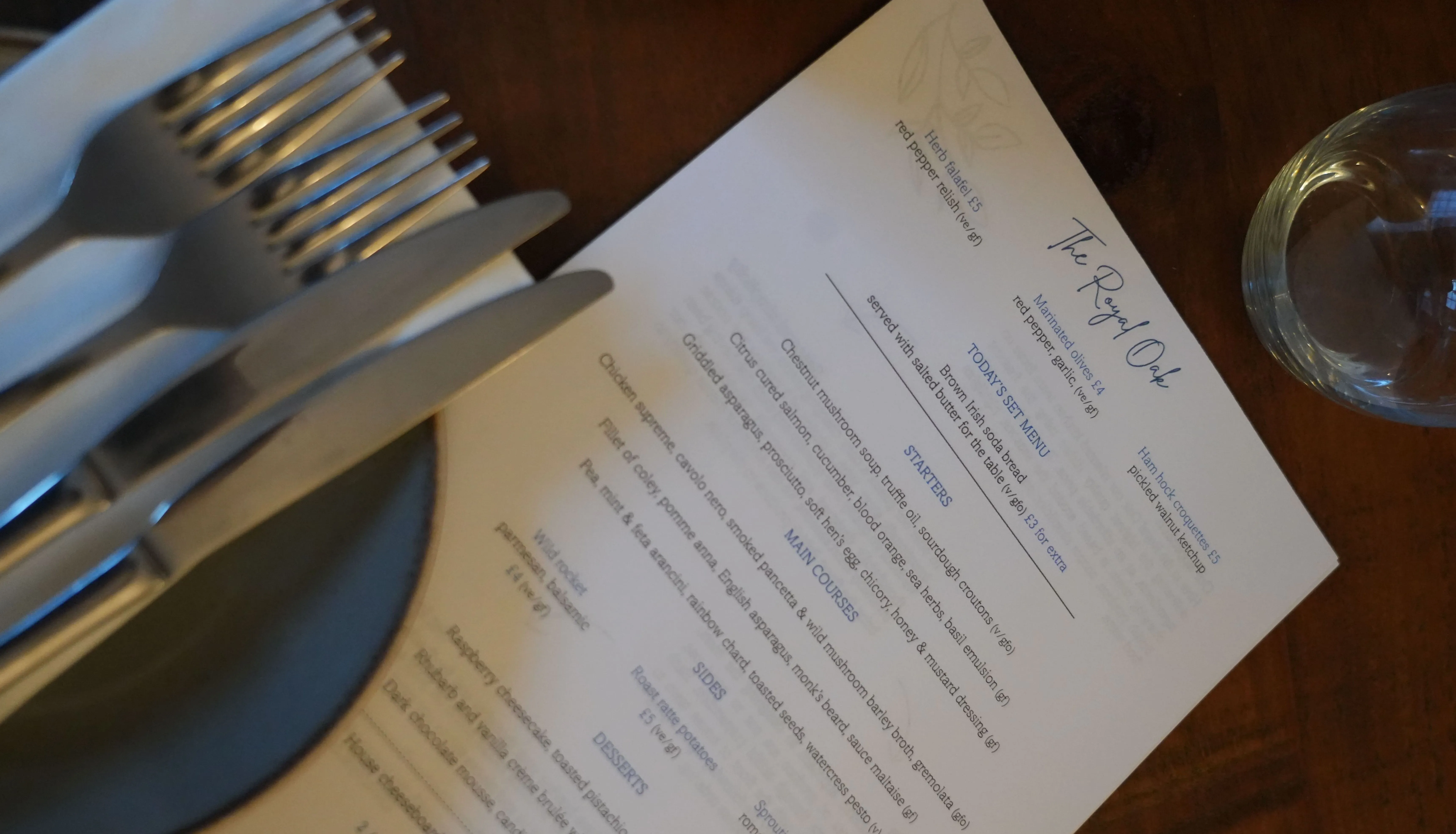 Restaurant table setting with stacked cutlery, a printed menu and a drinking glass.