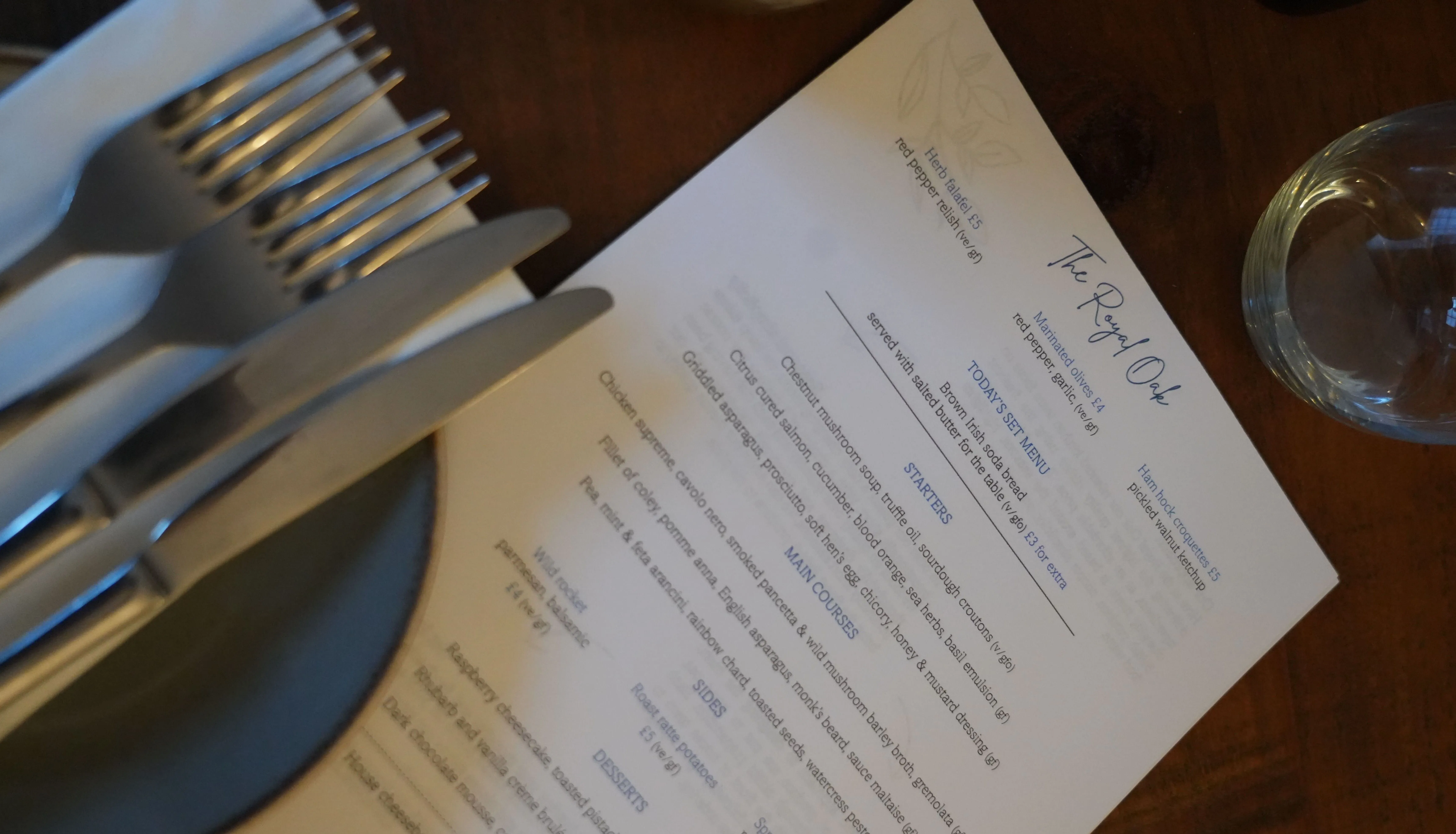 Restaurant table setting with stacked cutlery, a printed menu and a drinking glass.