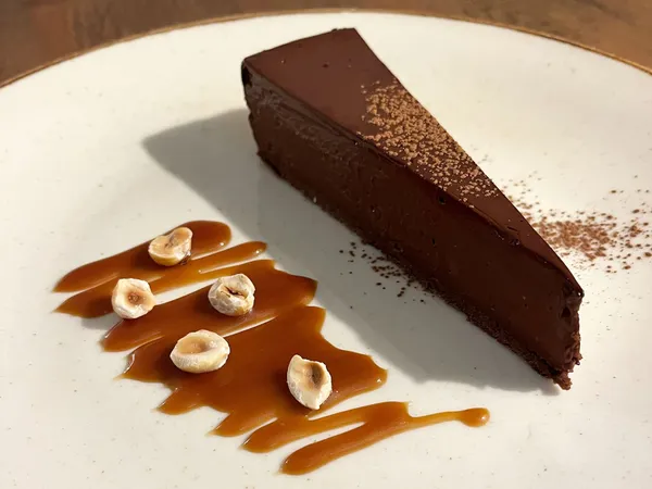 Slice of rich chocolate tart with caramel sauce and hazelnuts on a white plate