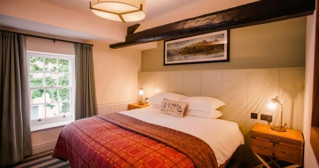 Cosy bedroom with a double bed, red patterned throw, exposed dark timber beam and warm bedside lighting.
