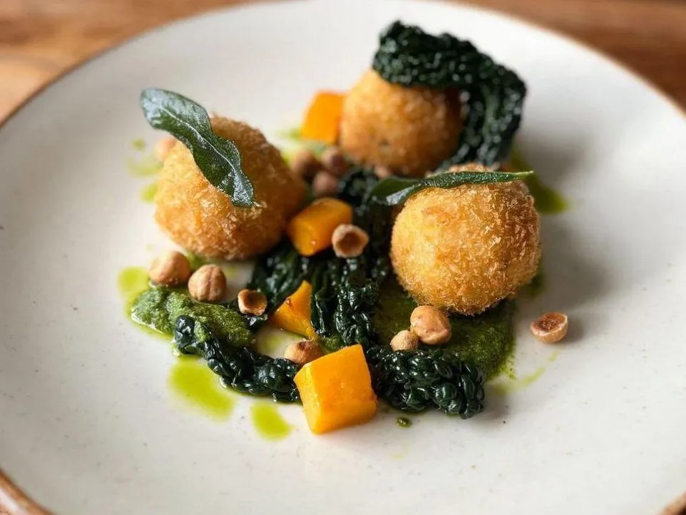 Gourmet plate of golden croquettes with black risotto, pumpkin cubes, hazelnuts and sage