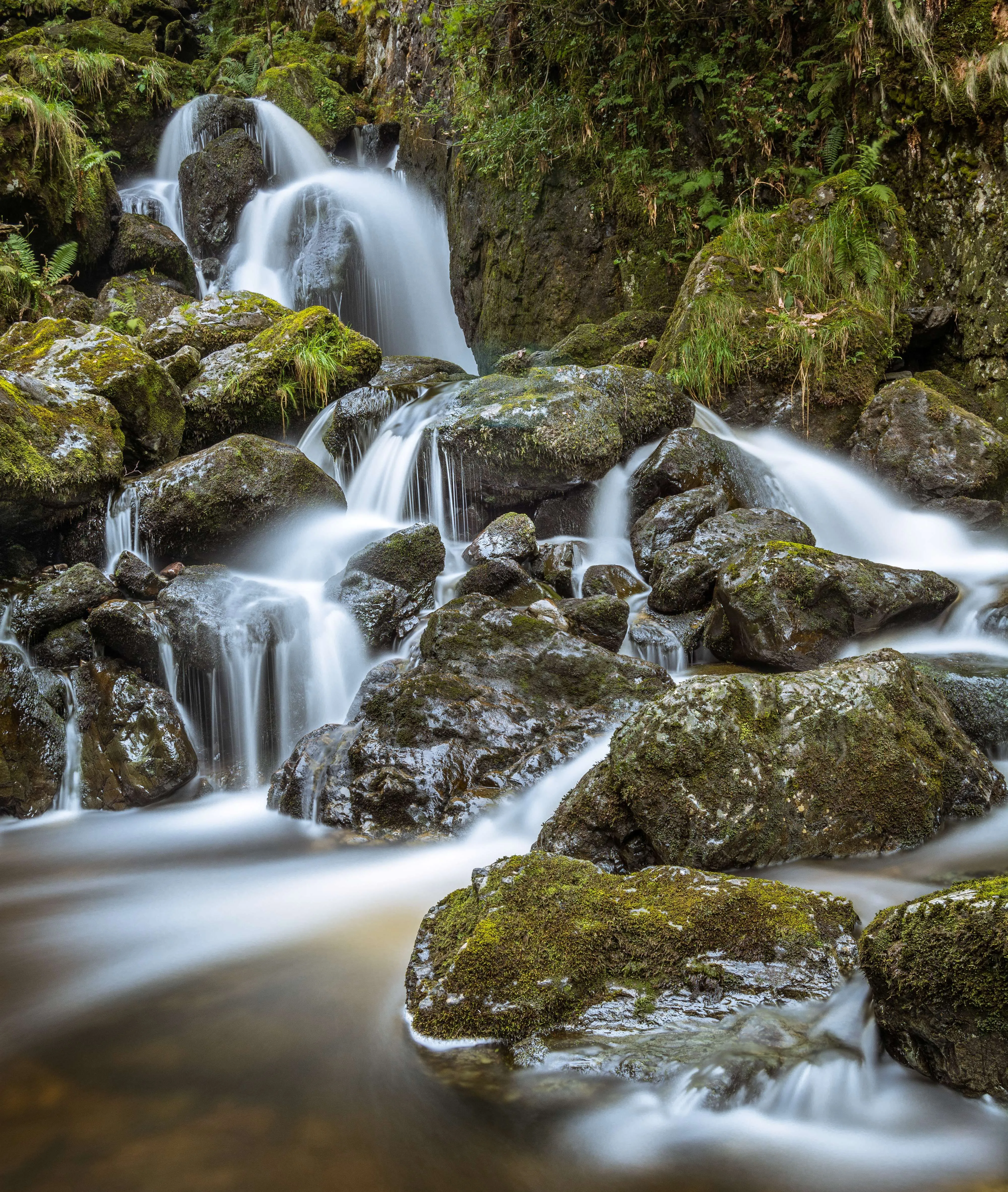 Long-exposure waterfall flowing over moss-covered rocks in a lush forest