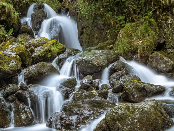 Long-exposure waterfall flowing over moss-covered rocks in a lush forest