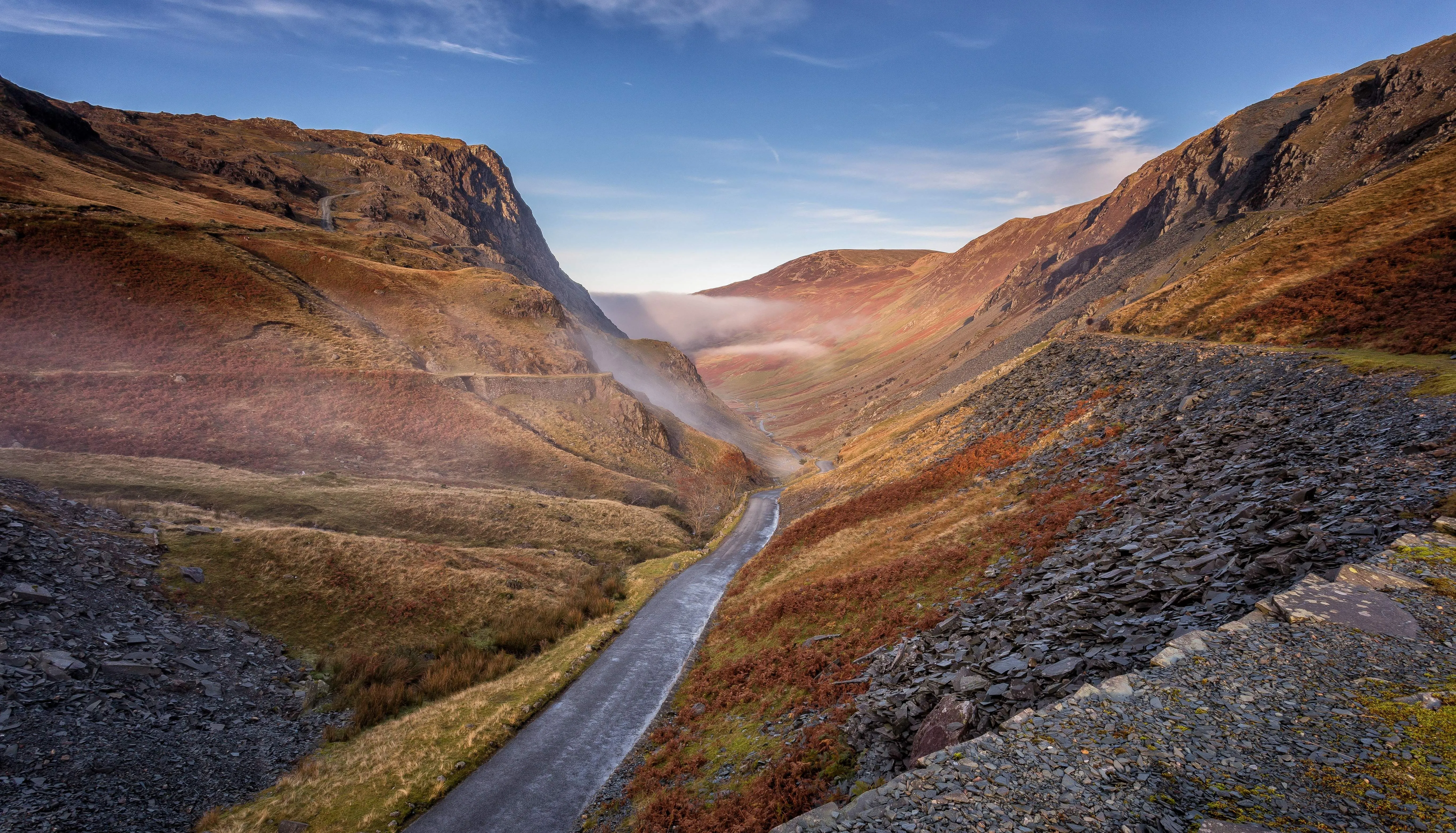 Winding mountain road through a misty rocky valley beneath a blue sky