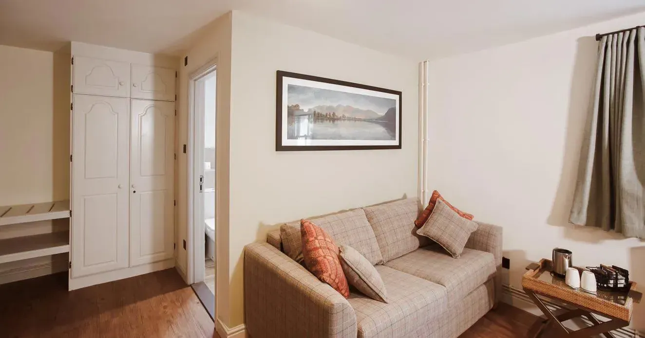 Cosy hotel suite sitting area with a beige sofa, cushions, tea tray and built-in wardrobe.