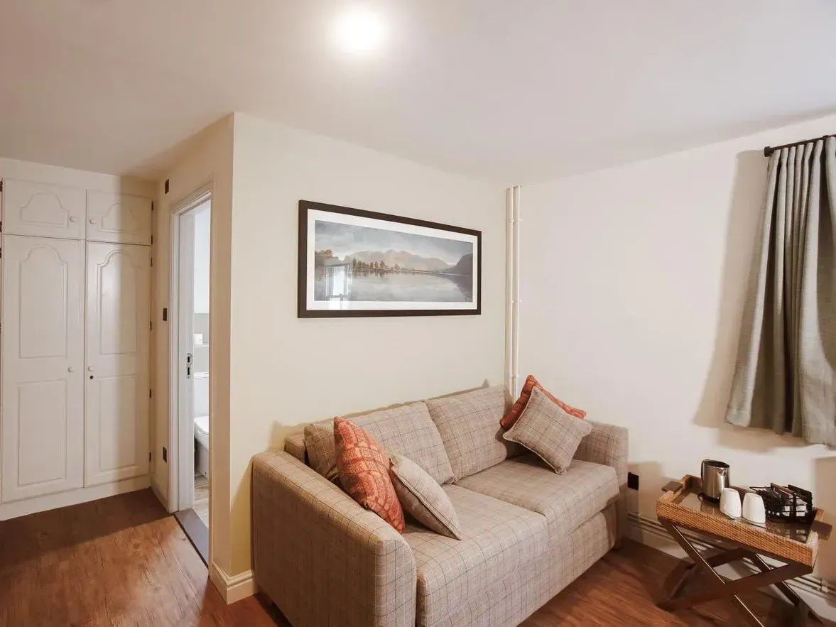 Cosy hotel suite sitting area with a beige sofa, cushions, tea tray and built-in wardrobe.