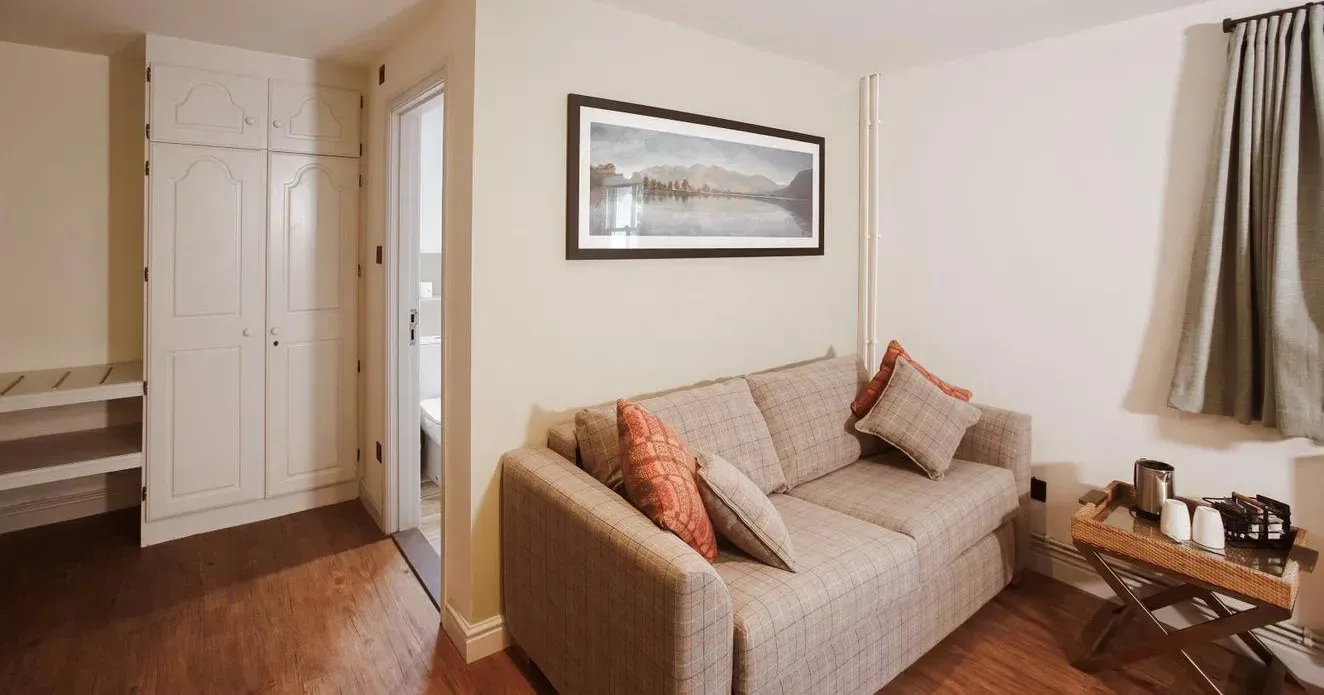 Cosy hotel suite sitting area with a beige sofa, cushions, tea tray and built-in wardrobe.
